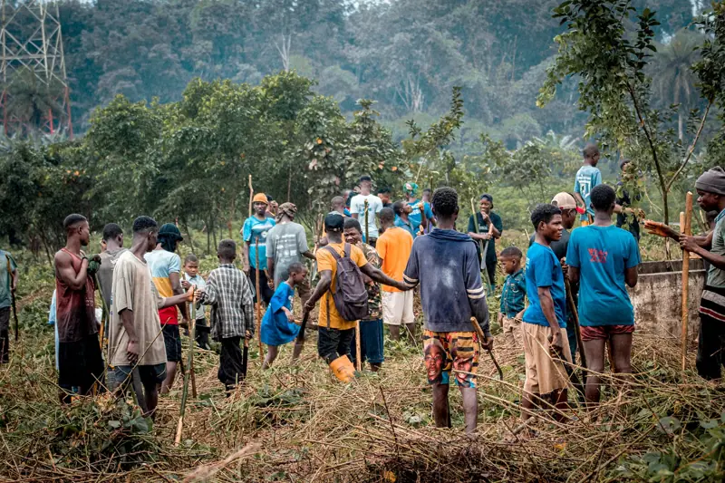 Young people gathered outdoors in a cleared field with forest behind them.